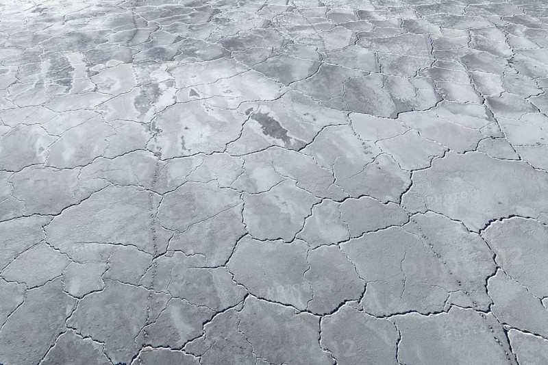 Aerial view of saline mud flats displaying a unique cracked surface pattern. The intricate texture forms naturally through the evaporation process in arid environments