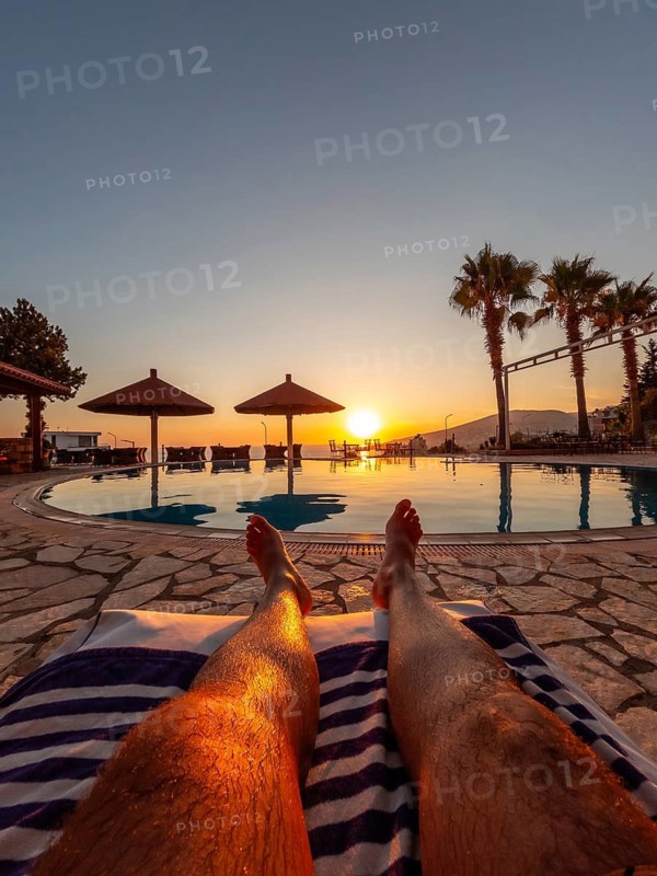 Feet of a man in a pool enjoying a sunset on summer vacation