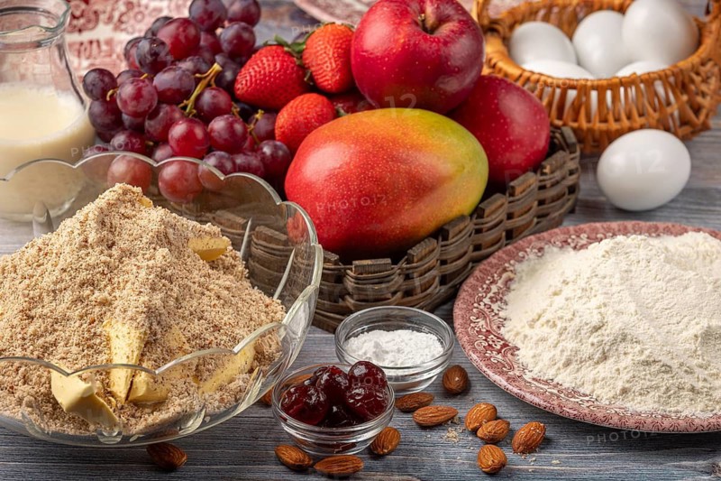 Bowl with baking ingredients next to eggs, milk and a basket of fruit