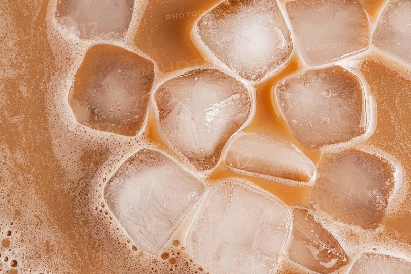 A detailed top-down view of iced cold brew coffee, showcasing ice cubes floating in the brew. The light brown coffee contrasts against the clarity of the ice, suggesting refreshment