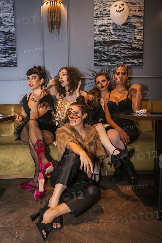 Halloween party with friends in a disco nightclub, portrait of a group of female friends sitting on a sofa in makeup and costumes