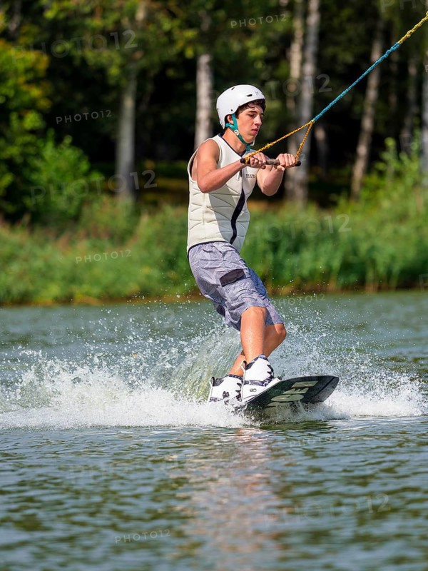Young man with wakeboard in lake, water sports, water skiing in wakepark