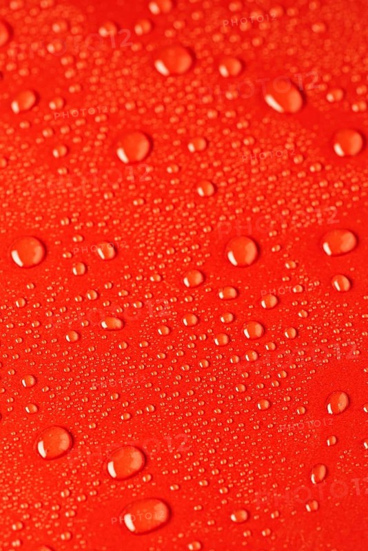 Close up of water droplets scattered on a vibrant red surface, creating a dynamic texture. The droplets vary in size, reflecting light beautifully. Ideal for backgrounds and design projects
