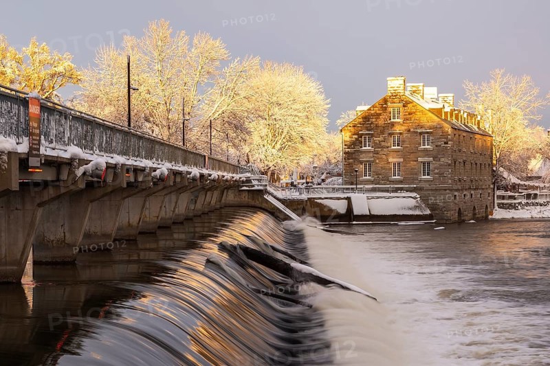 Moulin Neuf water flow control dam and walkway over Des Mille-Iles river plus New Mill on Ile des Moulins with first winter like snow in late autumn at sunset, Old Terrebonne, Quebec, Canada