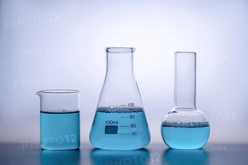 Three laboratory glassware items filled with a blue liquid sit on a reflective surface against a soft gradient background. The clean design emphasizes science and chemistry