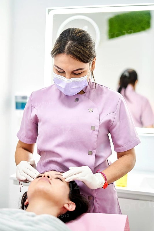 In a modern clinic of aesthetic medicine, a trained therapist performs a beauty treatment on a client. The environment is serene, focused on promoting relaxation and well-being
