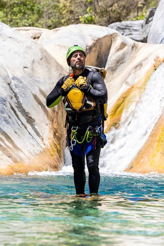 Man stands in shallow river in full canyoneering gear, surrounded by smooth rock formations and flowing water in Matacanes, Nuevo Leon. Nature and adventure unite