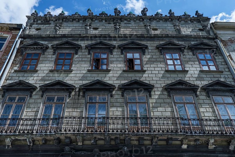 Dilapidated residential building with balcony and sculptures on the roof ledge, 19th century, Lemberg Ukraine