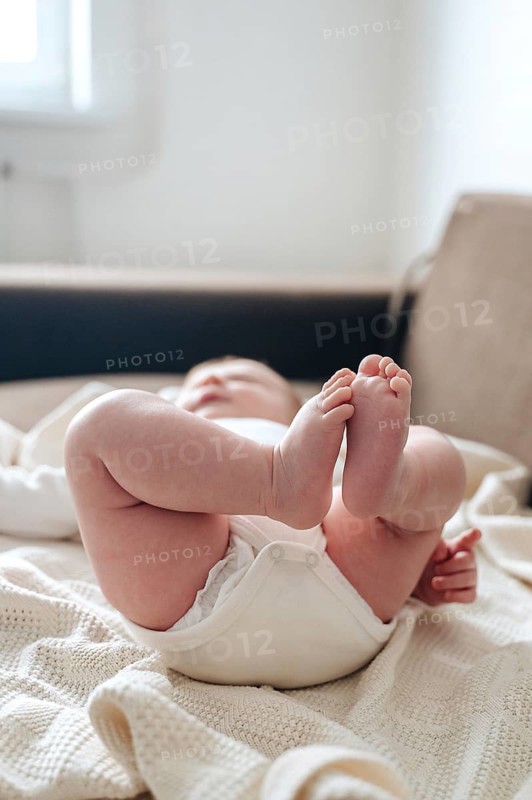 A serene image of a newborn baby girl lying on a soft, knitted blanket. Her tiny feet are playfully raised, capturing the innocence and warmth of infancy