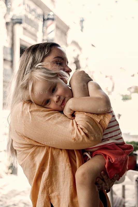 A loving mother embraces her young daughter outside. The mother holds her child gently, creating a warm and tender moment full of affection and care