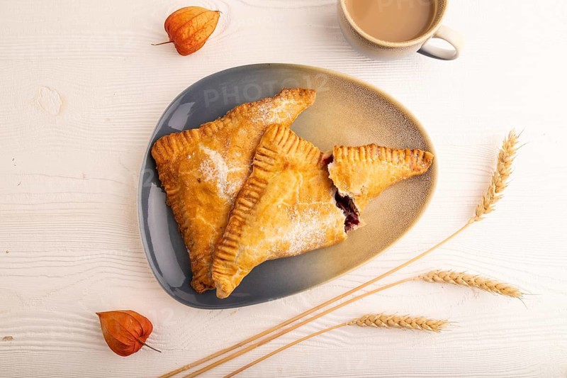 Triangles Pie, Puff Pastry, Samsa with cherry jam on white wooden background, cup of coffee, top view, flat lay, close up