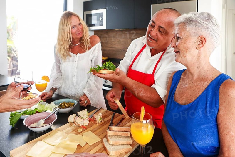 Joyful seniors gather at a vibrant kitchen party, sharing stories and laughter while indulging in food preparation. The serene setting buzzes with lively interactions and the warmth of good company