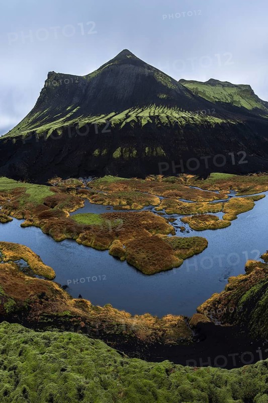 The breathtaking Icelandic Highlands showcase majestic dark mountains and lush green moss, enveloped by tranquil blue waters. A stunning portrayal of untouched nature's beauty