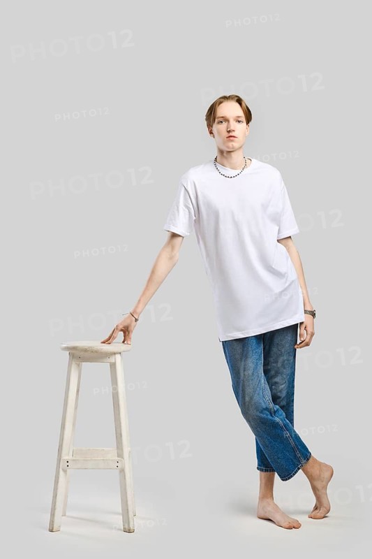 Full length portrait of young man in white t-shirt leaning to a sit of tall chair