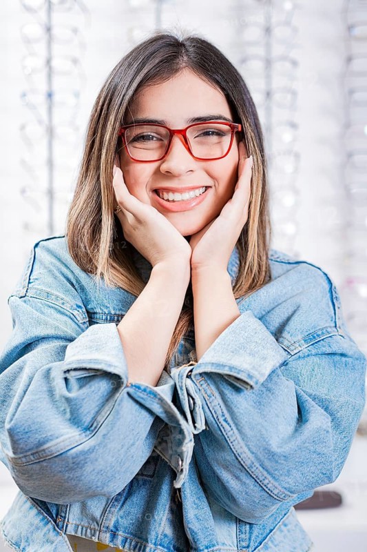 Happy female customer modeling glasses in an optical store. Happy teen girl in eyeglasses on a background of optical store