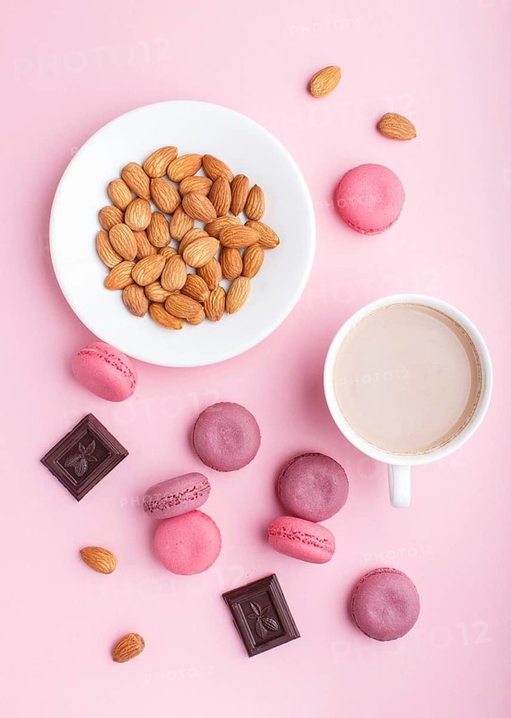 Purple and pink macaron or macaroon cakes with cup of coffee and almonds on pastel pink background. Morninig, spring, fashion composition. Flat lay, top view, pattern