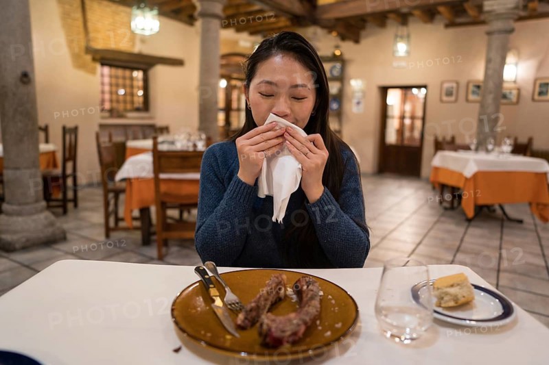 An Asian woman savors an Avila T-bone steak in a cozy restaurant. The warm ambiance enhances her dining experience, making it a memorable culinary delight