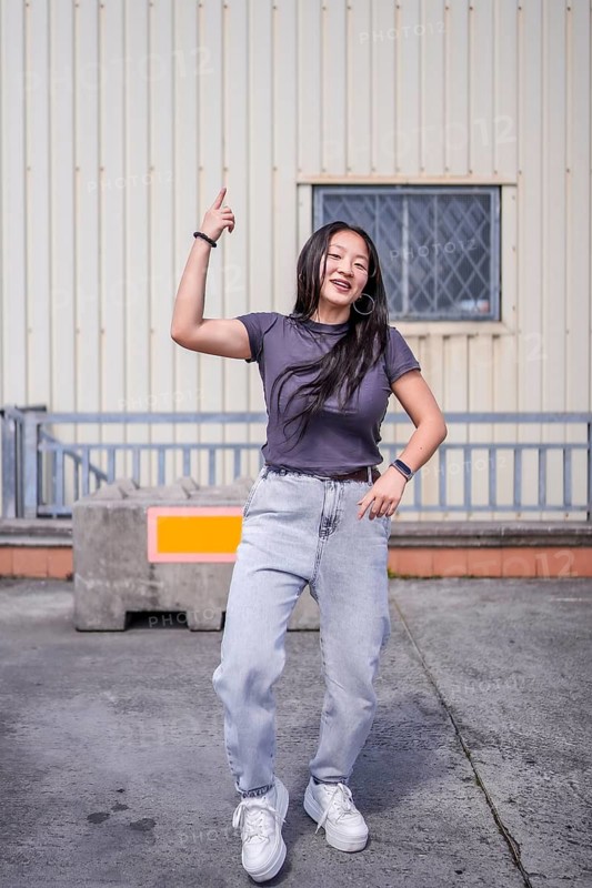 Vertical photo of a cool asian young woman dancing urban music outdoors next to an industrial building