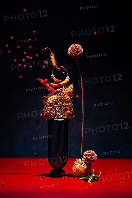 Dynamic display with chilies peppers and honeycomb on a black background. Floating red berries enhance the striking contrast and artistic flair