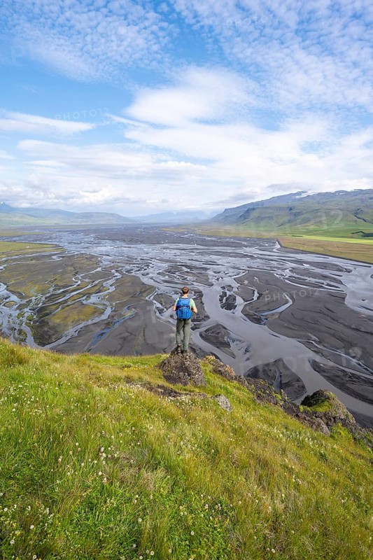 Hiker, young man on a hill, view over alluvial land, meandering river, Dímonarhellir, Suðurland, Iceland