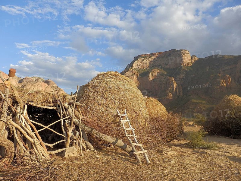 A rural village with piles of straw and mountains under a blue sky below the rock church of Abuna yemata Guh, Tigray, Ethiopia