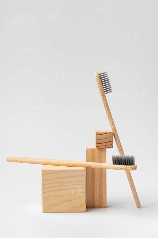 Two bamboo toothbrushes with black bristles are artistically arranged on natural wooden blocks, set against a neutral background. Ideal for eco-friendly and zero waste aesthetics
