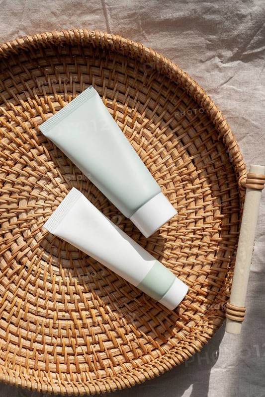 Two minimalist skincare cosmetics rest on a woven basket, basking in warm natural light. The simple design and natural texture create a serene and stylish look
