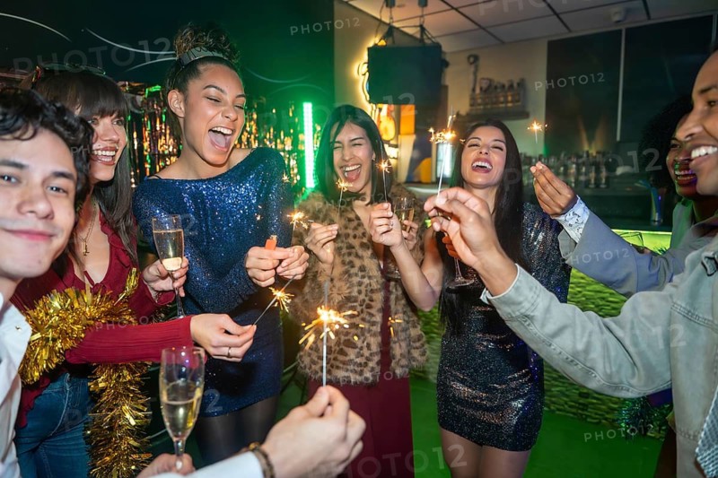 Group of happy diverse friends celebrating a special event, enjoying sparkling fireworks and toasting with glasses of champagne in a dimly lit bar or club