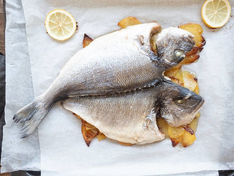 Delicious oven-baked dorado fish with sliced potatoes and lemon on parchment paper