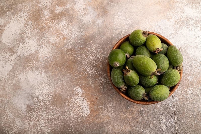 Ripe Feijoa in wooden bowl on brown concrete background, top view, flat lay, copy space, minimalism