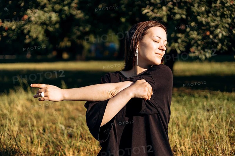 A teenage girl enjoys a peaceful morning in the garden, stretching her arms and embracing the tranquility of nature. The sunlight gently illuminates her content expression