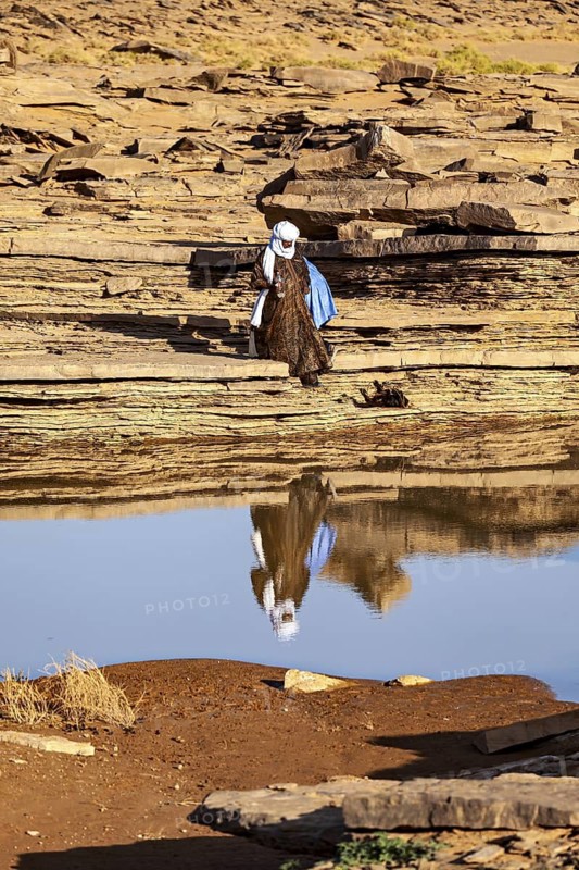 Person in traditional dress moving over rocks near a waterhole, Tuareg fetching water in the Sahara in Algeria