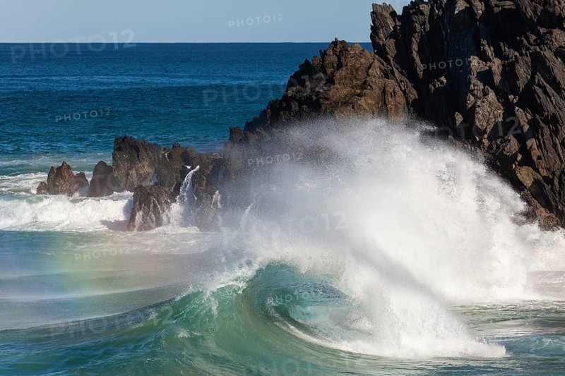 Waves crash against rocks at the mainland's easternmost point, creating rainbows in the ocean spray. Daylight, Byron Bay, New South Wales, Australia