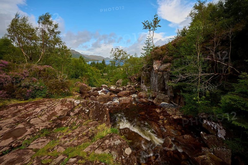 Water flows over rocks in a wooded area under blue skies, Victoria Falls, Slattadale, Achnasheen, Scotland, United Kingdom, Great Britain