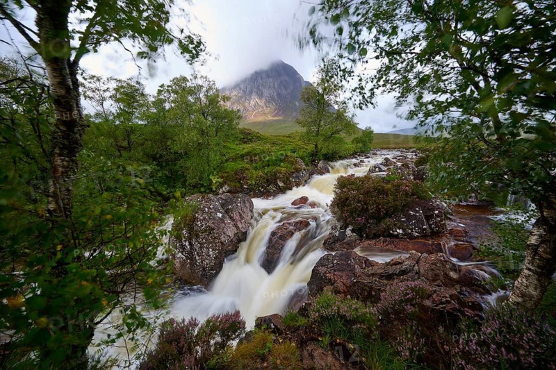 Beautiful waterfall surrounded by green vegetation with an imposing mountain in the background and dramatic sky, Buachaille Etive Mor Viewpoint, River Coupall, Glen Etive, Scotland, United Kingdom, Great Britain