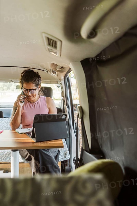 A woman enjoys remote work inside a cozy van during autumn in New Zealand. The setup includes a laptop, phone, and comfortable seating, embodying the freedom of van life