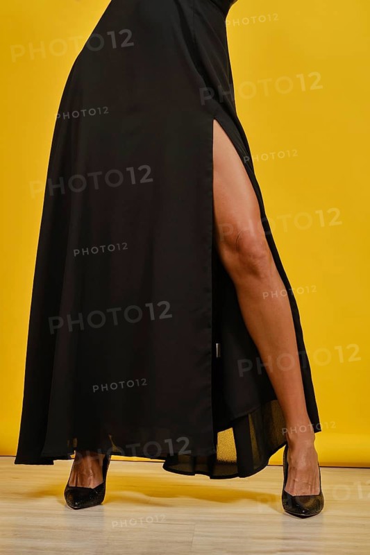 Unrecognizable woman in a stylish black high-slit dress show her long slender leg with tan skin