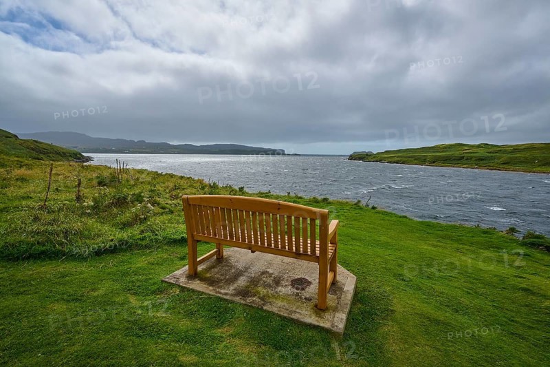 Wooden bench overlooking sea surrounded by green meadow and cloudy sky, Isle of Skye, Scotland, United Kingdom, Great Britain