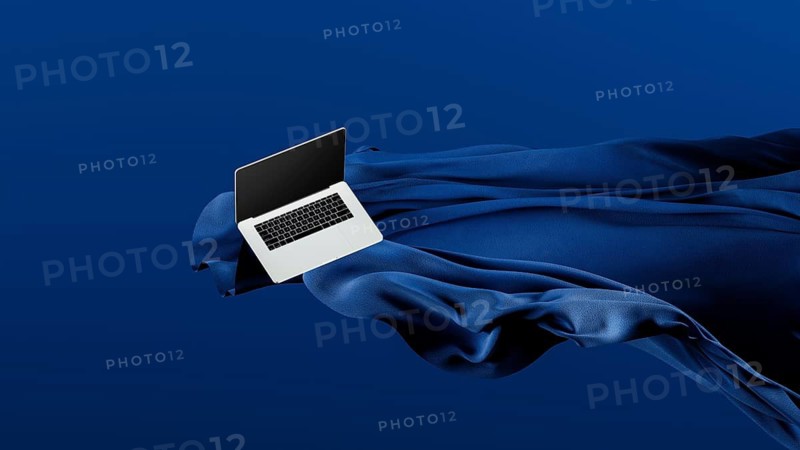 A sleek laptop is placed atop smooth fabric, showcasing its lightweight design against a rich blue backdrop