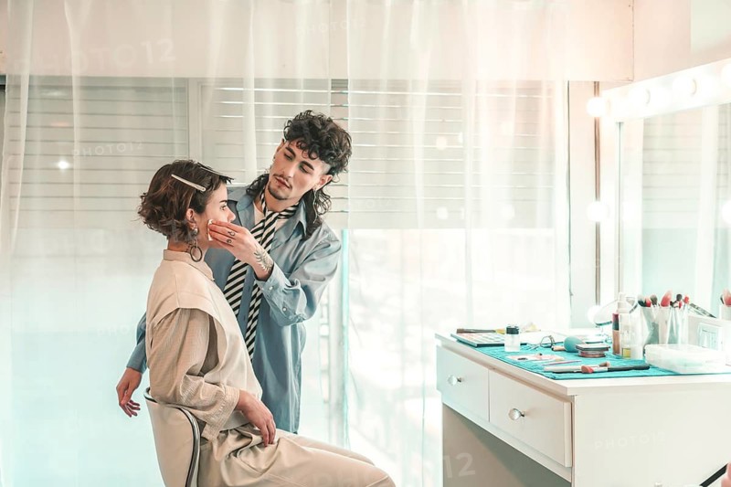 Professional makeup artist carefully applying foundation on a model's face, preparing her for a photoshoot or event in a bright and modern beauty salon