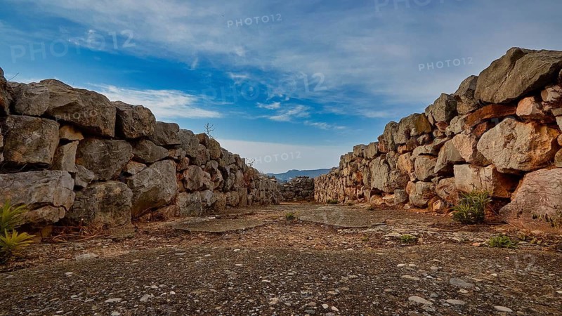 Path between high stone walls with a view of blue sky and distant mountains, Tiryns, ancient city in Argolis, Mycenaean, Peloponnese, Greece