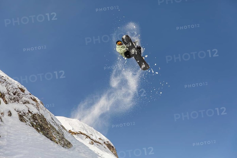 A dynamic image of a freeride snowboarder soaring through the air against a clear blue sky. Snow powder splashes around as the athlete embraces winter adventure in the mountains