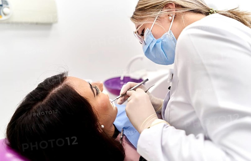 A dentist wearing protective gear examines a patient's teeth in a modern dental clinic. The focus is on providing professional dental care and ensuring patient comfort and safety