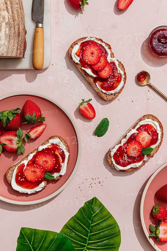 Top view of a delicious summer breakfast featuring toasted bread with cream cheese, strawberry slices, and jam. Ideal for brunch or a homemade snack