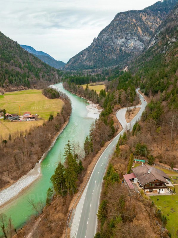 Aerial view of a winding Saalach river next to a road with surrounding forest and mountains under a cloudy sky, Bad Reichenhall, Bavaria, Germany