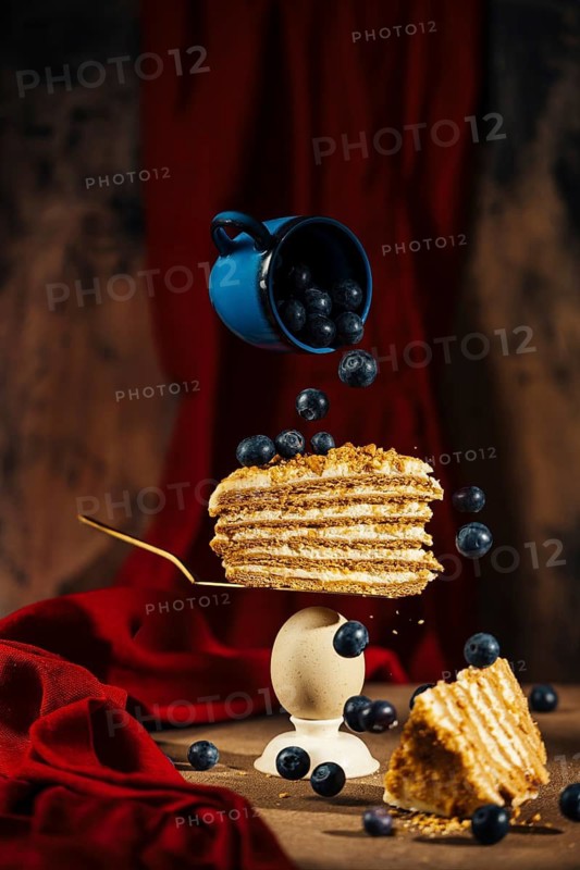 A stunning visual capture showcasing a slice of layered cake speared on a fork, suspended with blueberries seemingly defying gravity, set against a plush red background