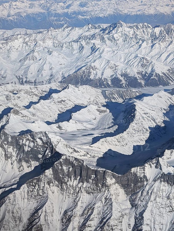An aerial perspective reveals a breathtaking scene of rugged, snow-covered mountains, with sharp peaks and deep valleys creating an awe-inspiring natural panorama