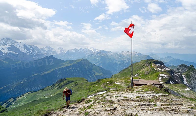 Hikers next to Swiss national flag at the summit of Faulhorn, mountain panorama with Eiger, Mönch and Jungfrau in the back, Bernese Alps, Bernese Oberland, Switzerland