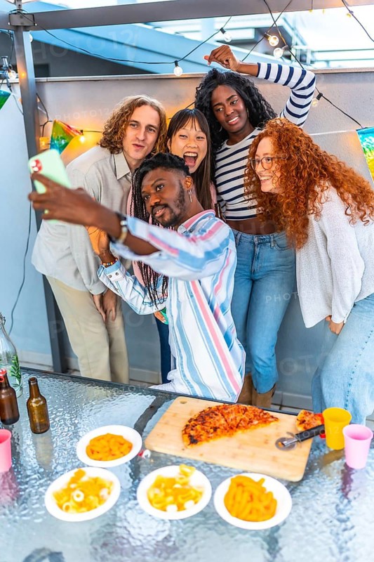 Vertical photo of a happy multi-ethnic friends taking selfie while celebrating a party at rooftop
