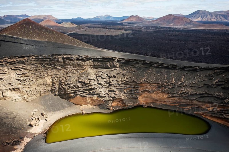 Aerial view of Playa de los Clicos in Lanzarote showcasing the unique volcanic terrain and a striking green lagoon amidst rugged volcanic cones
